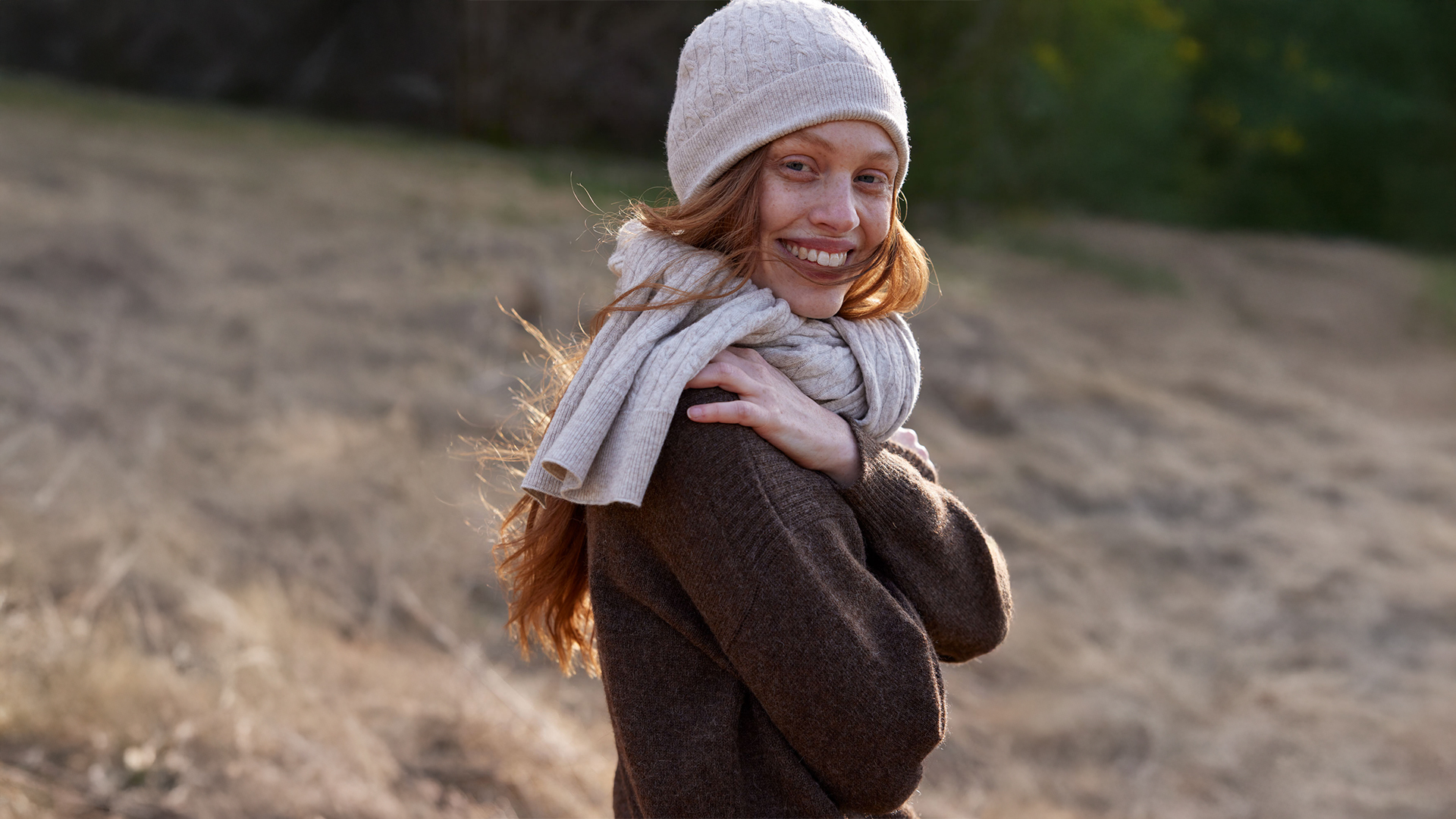 Lächelnde Person mit Mütze und Schal im herbstlichen Feld