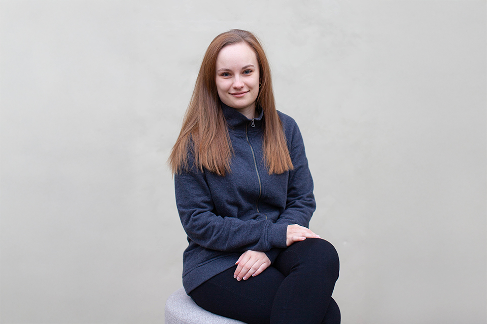 Junge Frau sitzt ruhig mit gefalteten Händen vor hellem Hintergrund