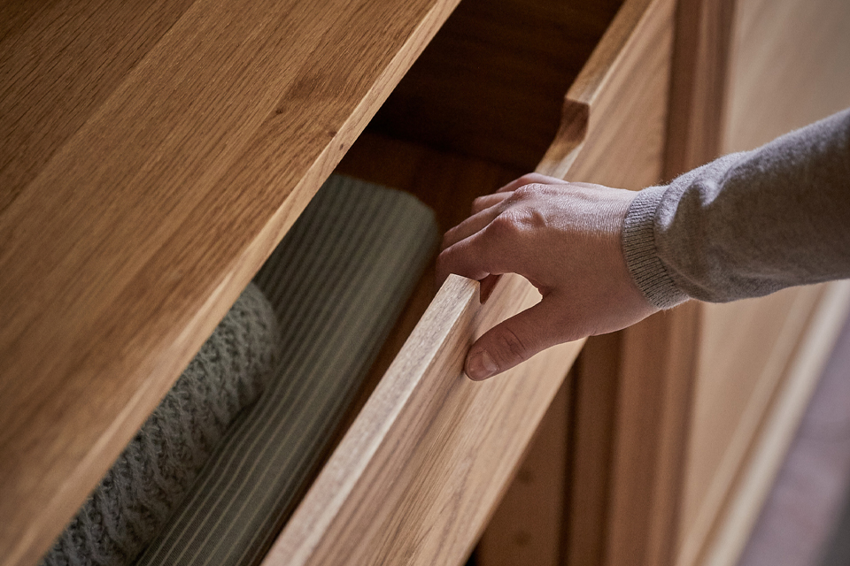Hand öffnet Holzschublade mit gefalteter Kleidung