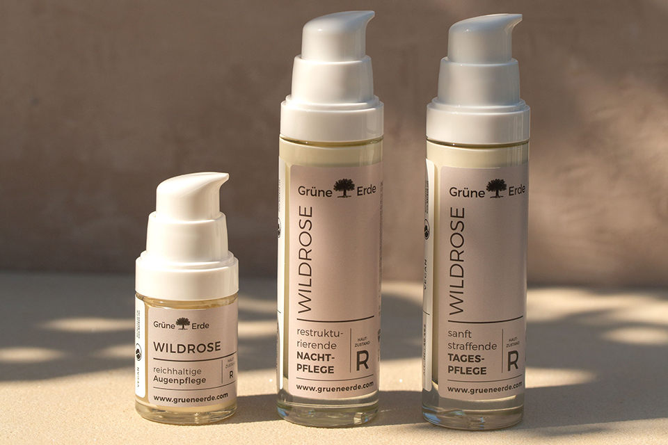 Drei Wildrose Hautpflegeflaschen mit Pumpspendern auf heller Oberfläche.