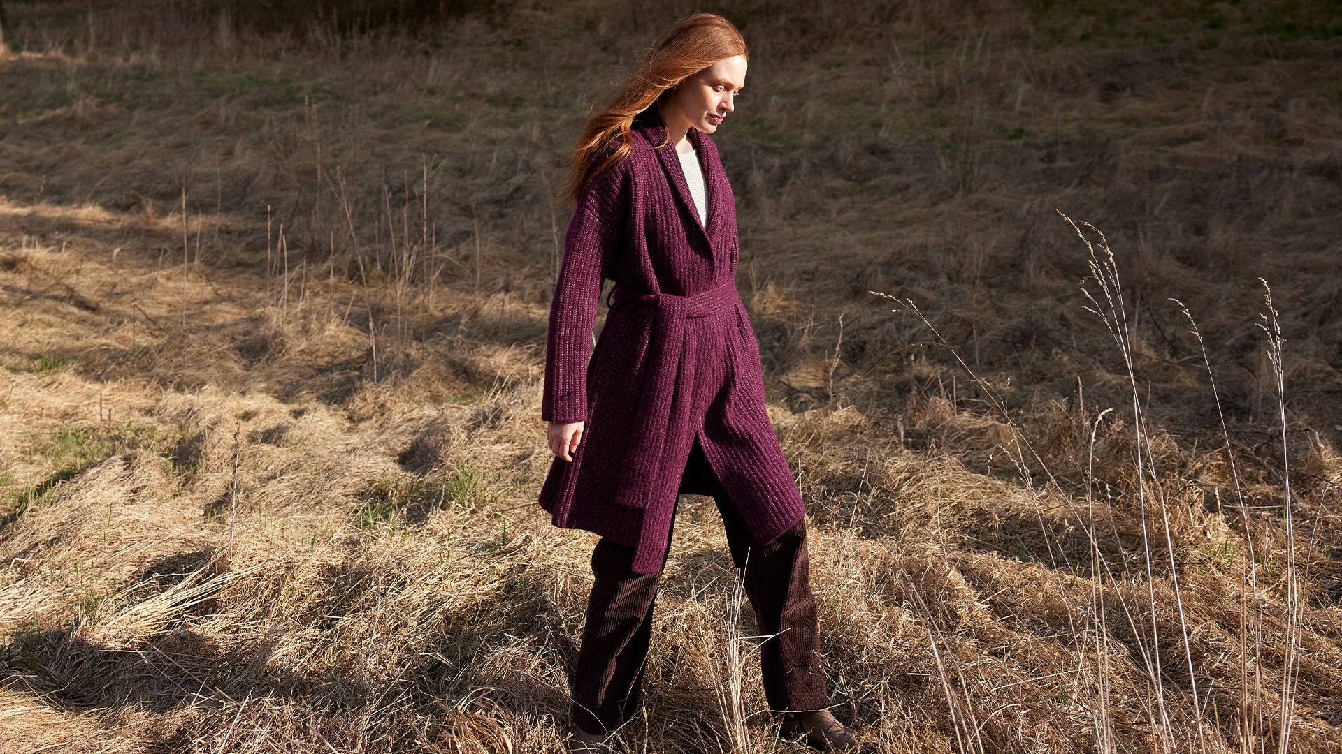 Frau in weiter Strickmode spaziert durch trockene Landschaft