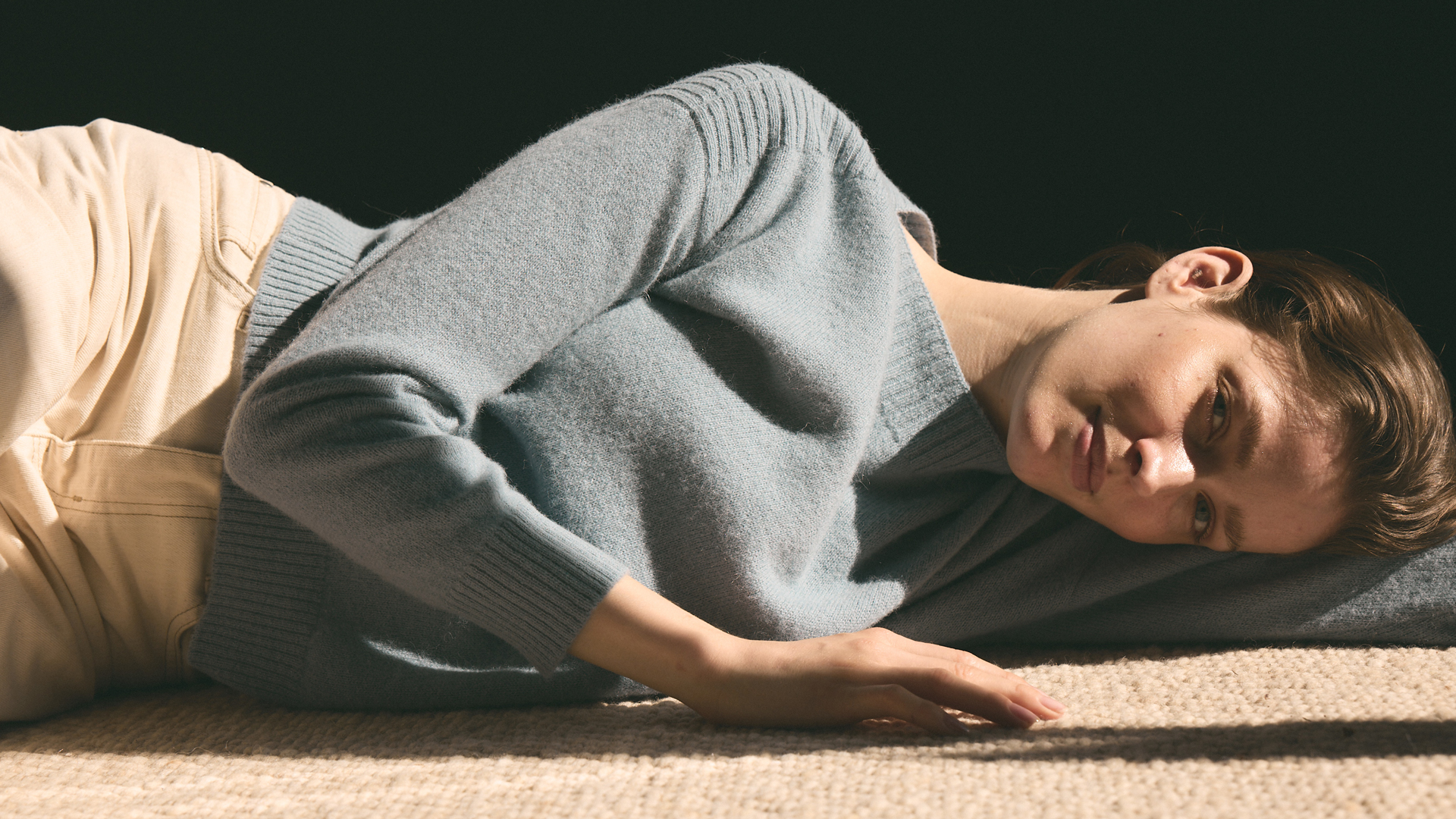 Frau liegt entspannt in heller Kleidung auf weichem Untergrund