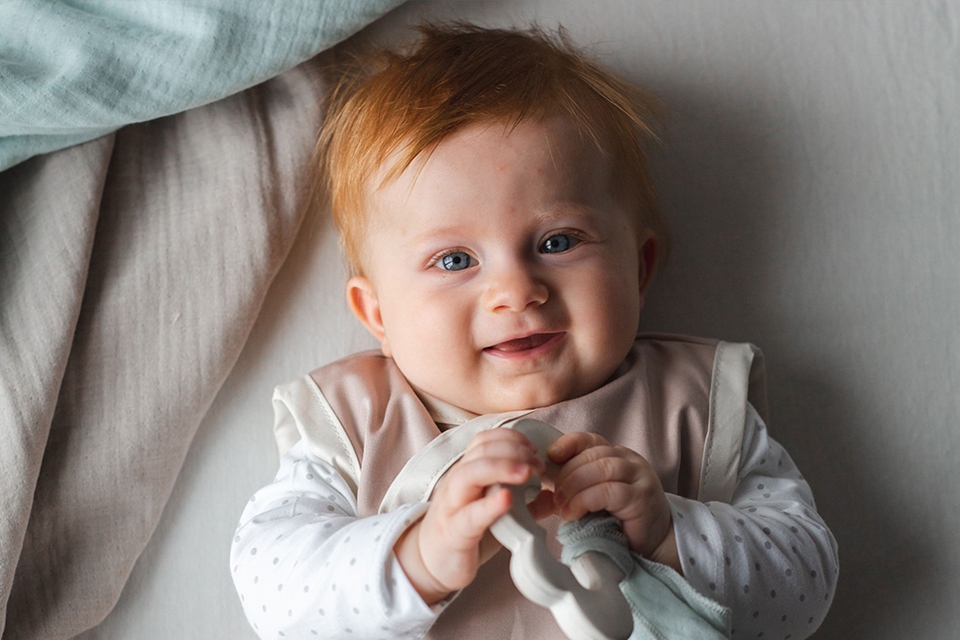 Spielendes Baby mit Holzrassel lächelt in die Kamera