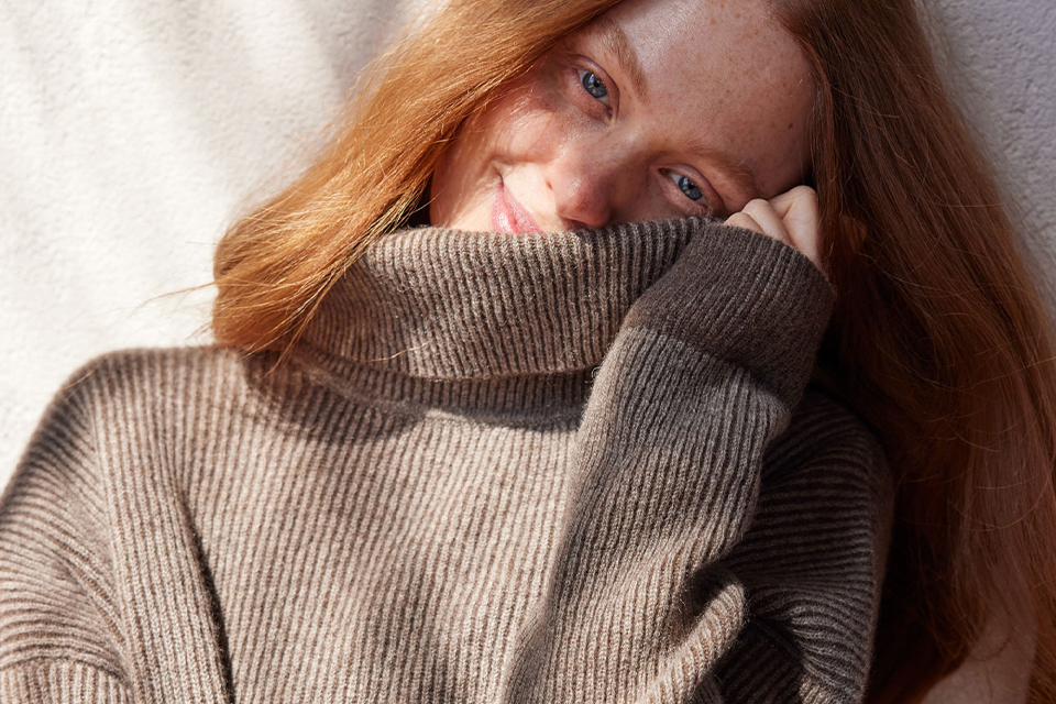 eine Frau in einem braunen Pullover neigt ihren Kopf zur Seite