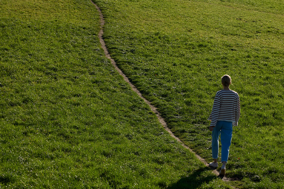 Person geht allein auf schmalem Pfad durch grüne Landschaft