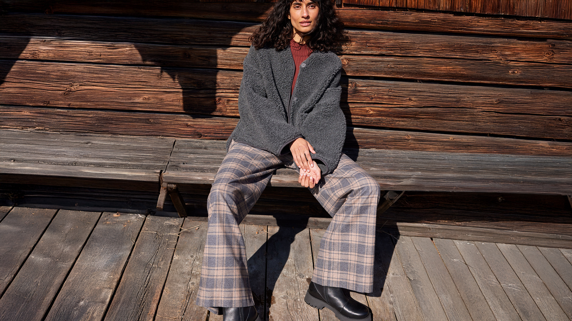 Frau sitzt entspannt vor Holzwand in moderner Kleidung