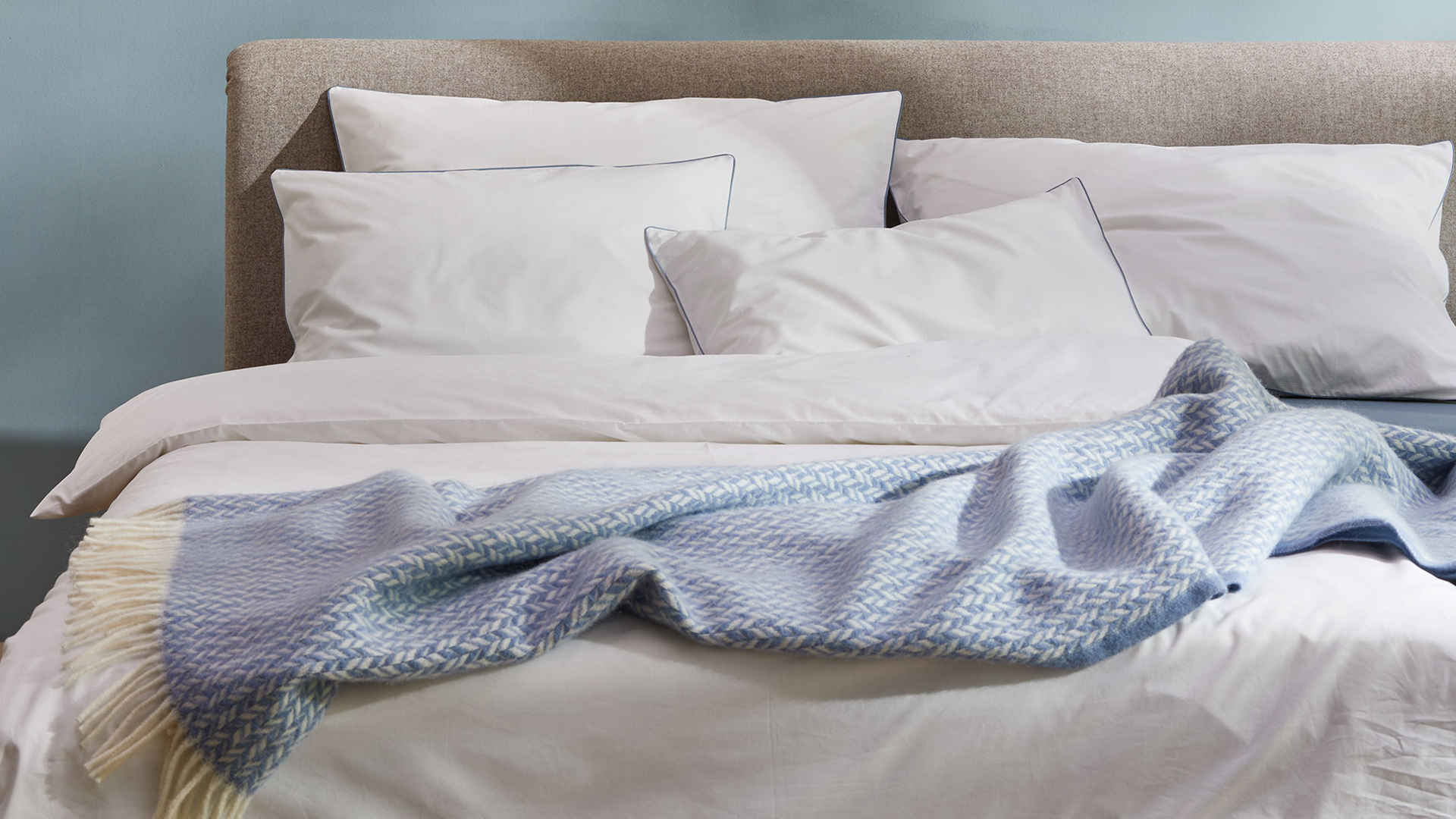 Blaue Wohndecke liegt auf weißer Bettwäsche auf einem Bett