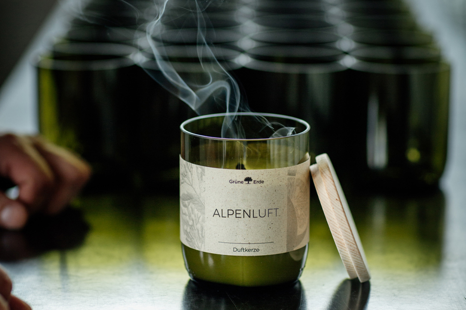 Grüne Kerze mit verglühendem Docht vor leeren Kerzengläsern stehend