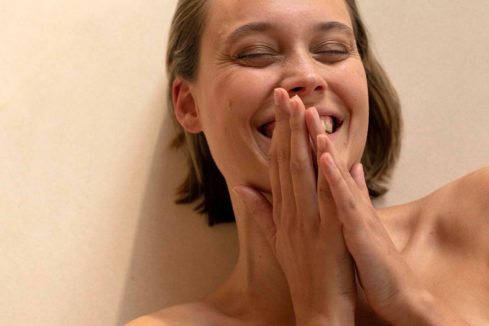 Lachende Frau bedeckt ihr Gesicht mit Händen und wirkt entspannt