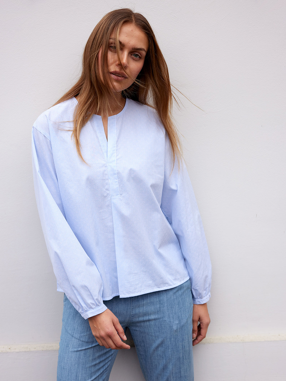 Frau vor weißer Wand in hellblauer Bluse und blauer Jeans