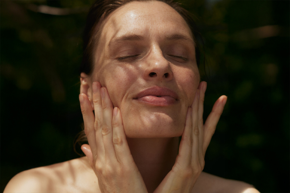 Frau mit geschlossenen Augen trägt Gesichtspflege auf
