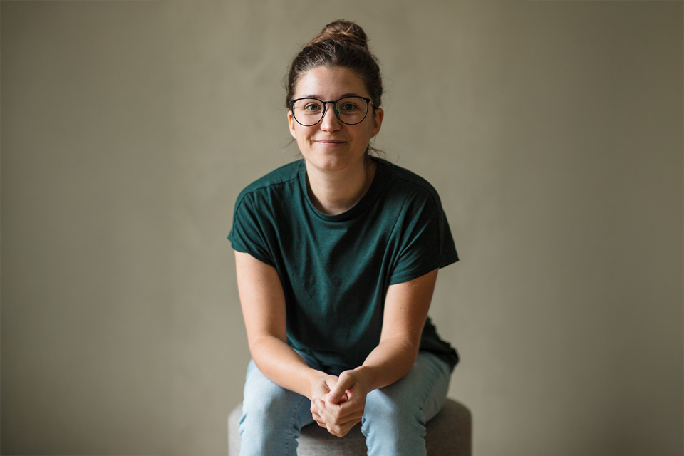 Frau mit Brille sitzt locker und lächelt in die Kamera