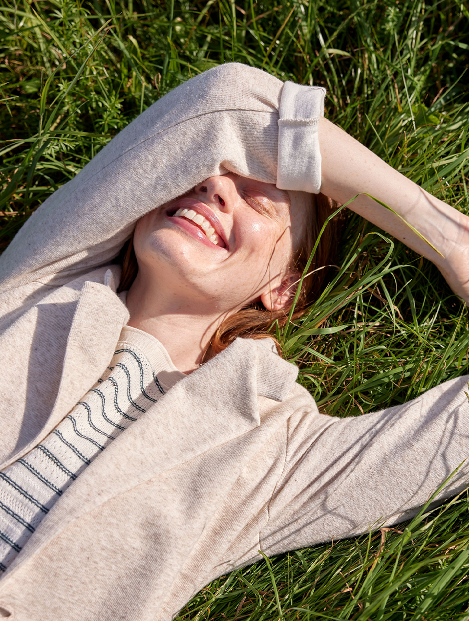 Frau im gestreiften Shirt und beigem Jäckchen liegt lachend auf einer Wiese