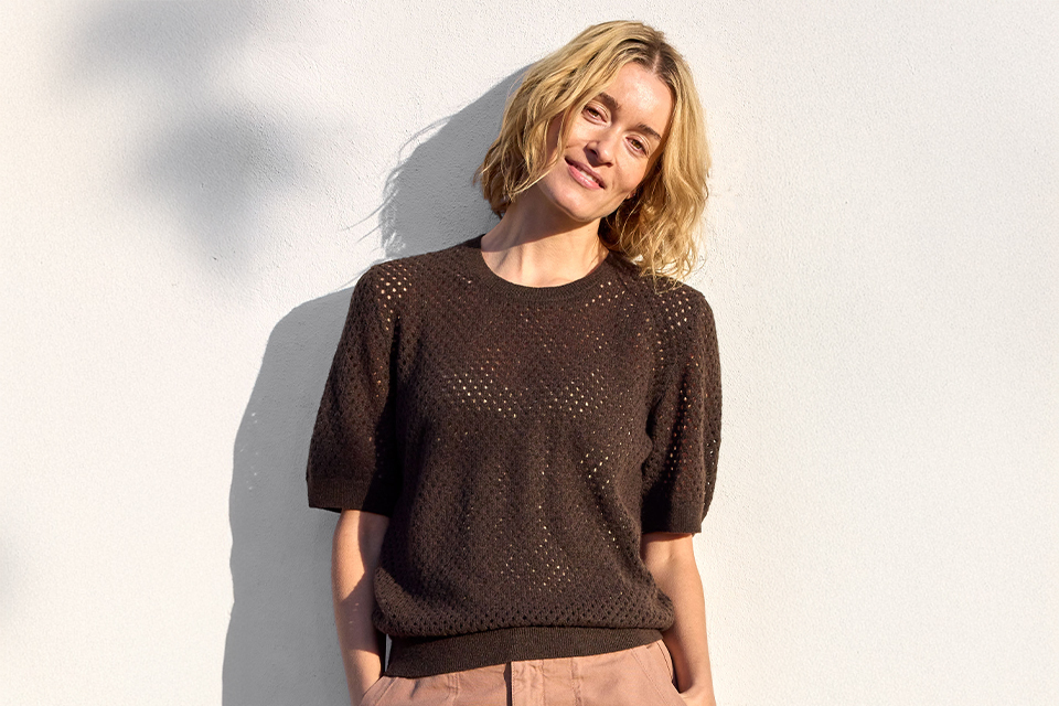 Frau mit kurzen Haaren trägt dunkles Oberteil und lächelt