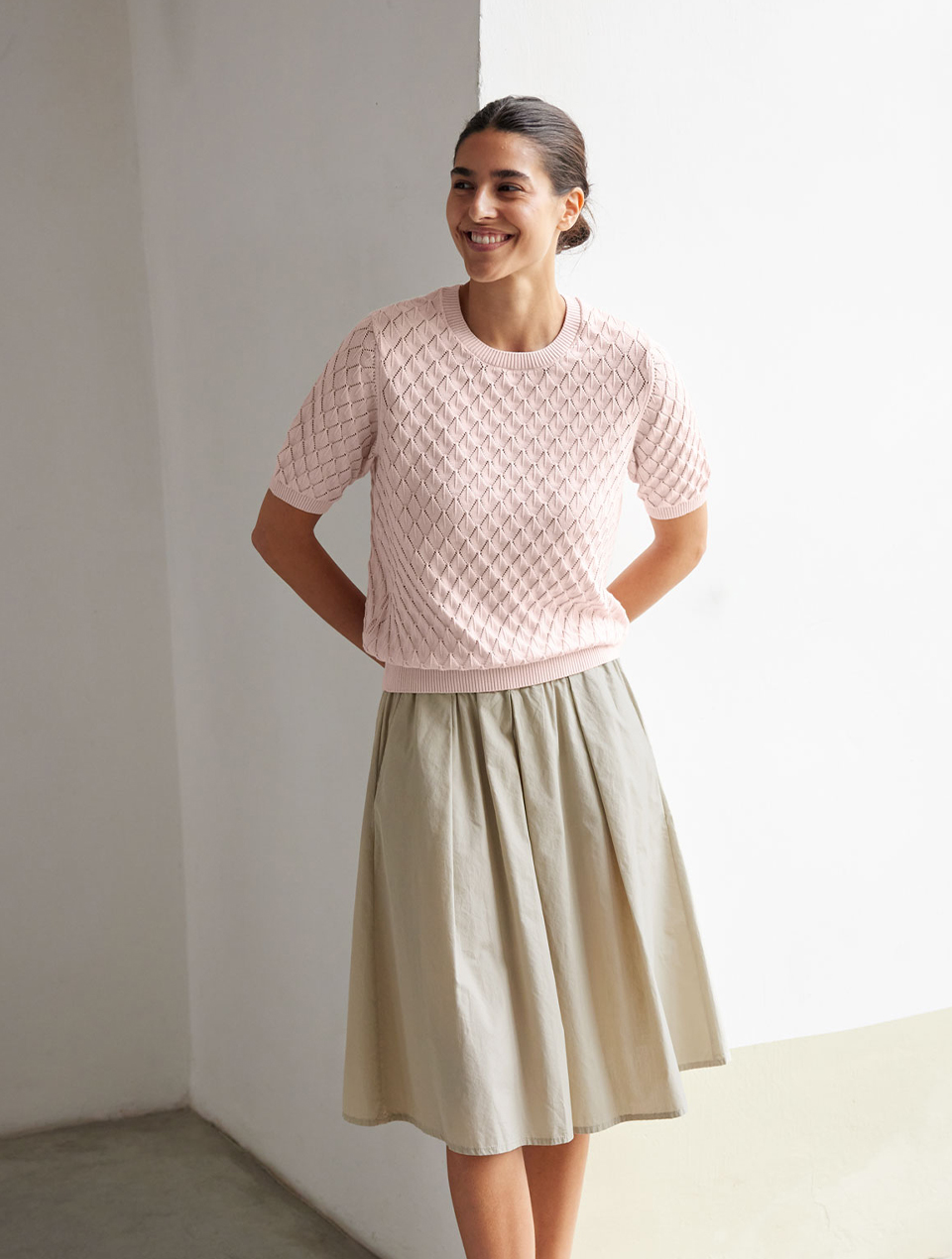 Frau im rosa Oberteil und beigem Rock steht in hellem Raum