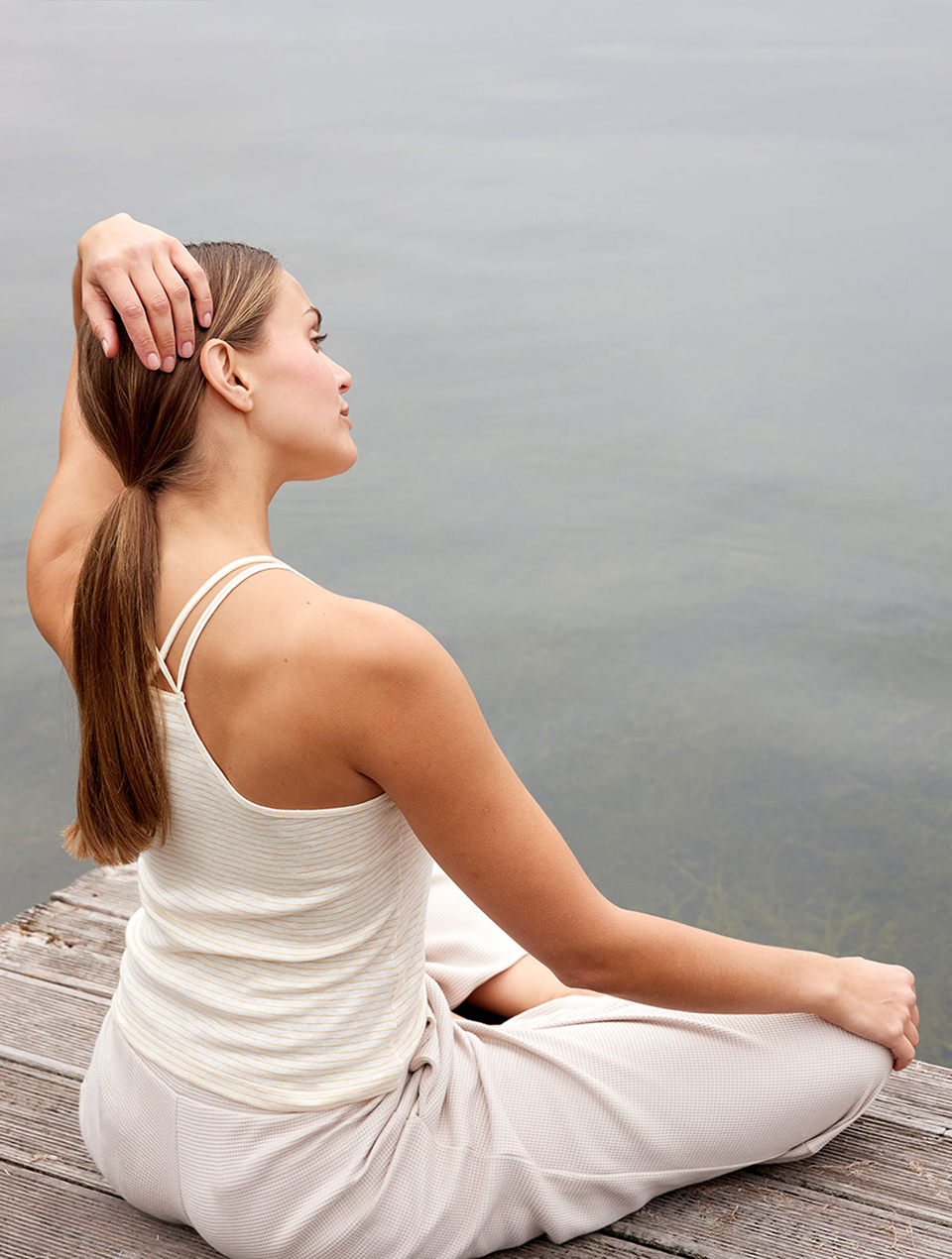 Frau sitzt am Wasser und trägt helles Trägertop und Yogahose