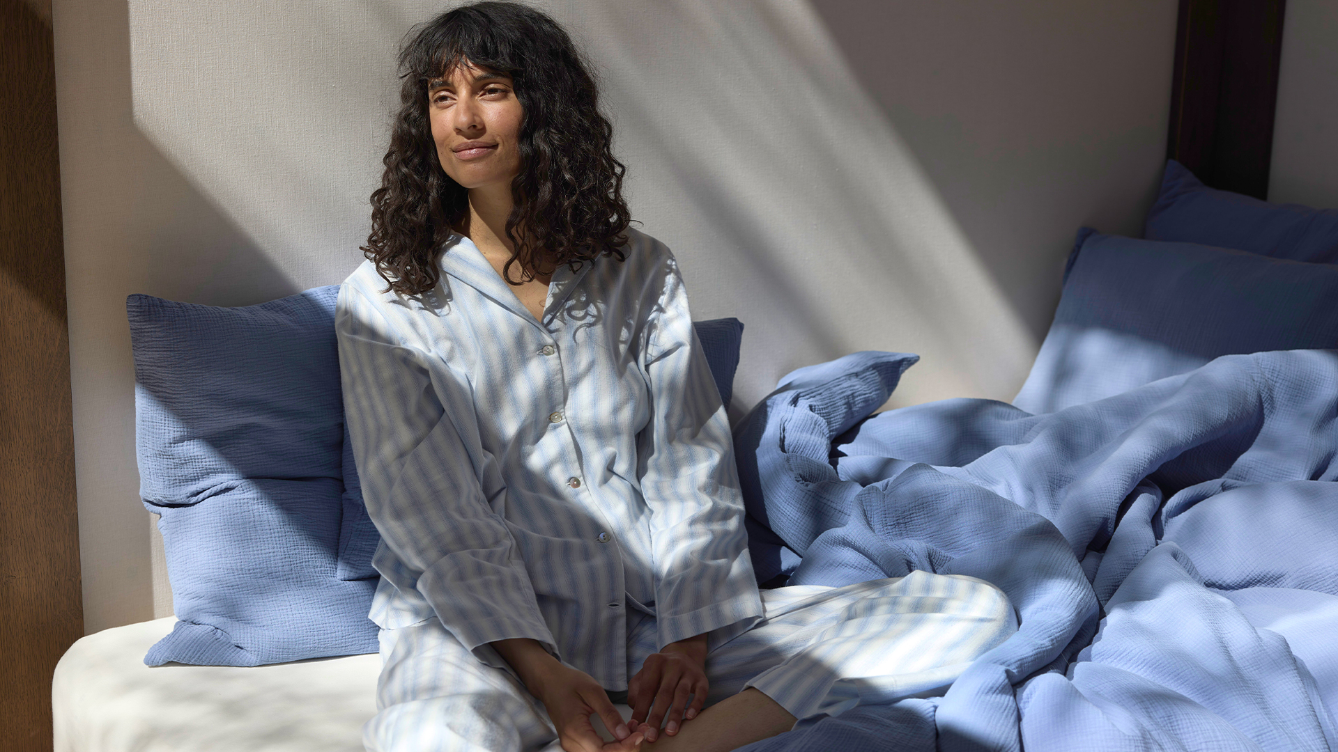Eine Frau in blau weiß gestreiftem Pyjama sitzt auf einem Bett mit blauer Bettwäsche