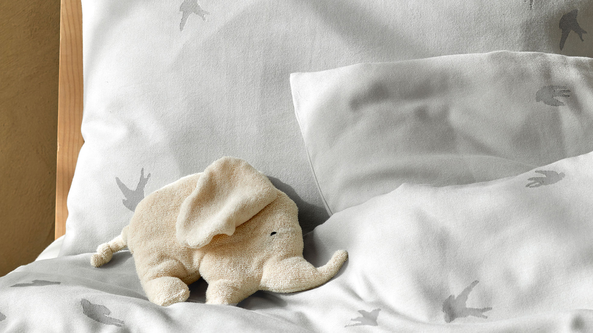 Weiße Bettwäsche mit einem kleinen Kuscheltierelefanten auf einem Bett