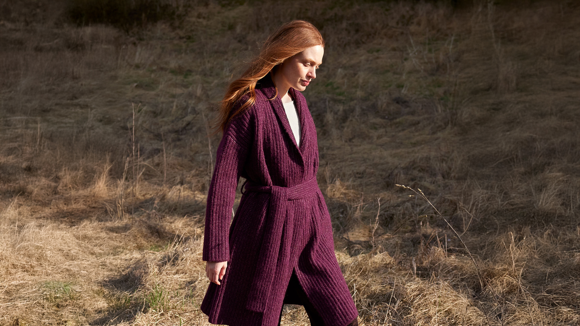 Frau in weiter Strickmode spaziert durch trockene Landschaft