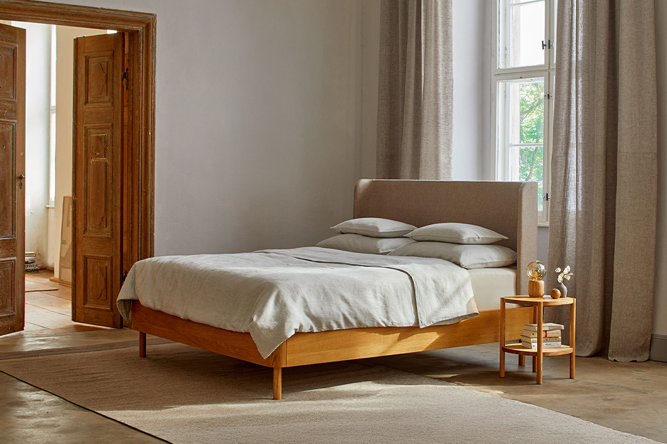 Helles Schlafzimmer mit Holzbett und weichen Textilien in natürlichen Farben