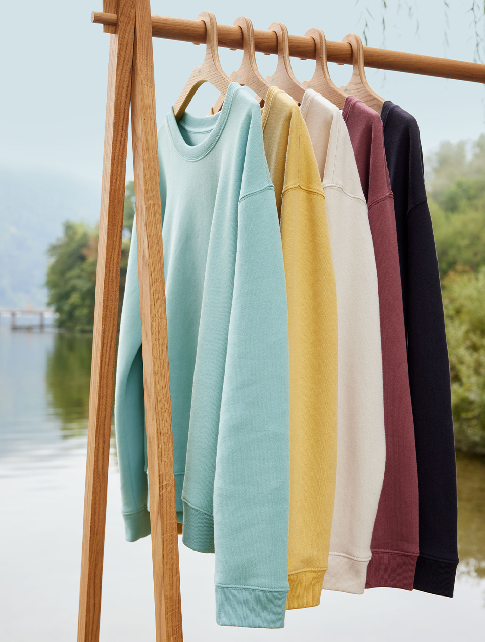 Mehrere Sweatshirts in verschiedenen Farben hängen auf einer Kleiderstange in natürlicher Umgebung