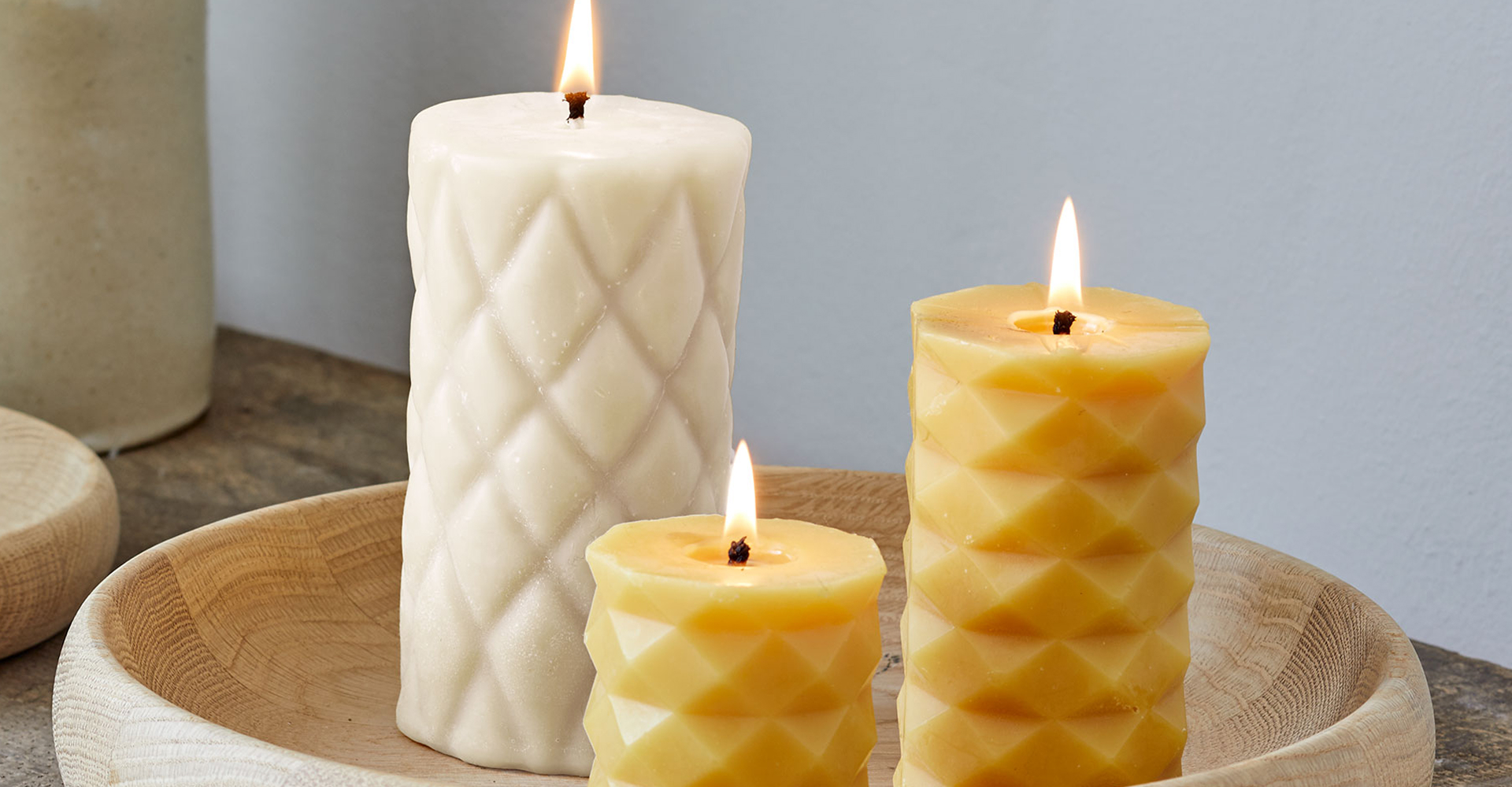 Zwei gelbe und eine weiße Kerze stehen auf einem Holztablett.