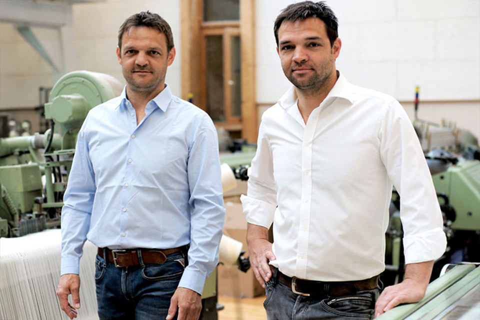 Zwei Männer stehen in einem Raum mit Webmaschinen