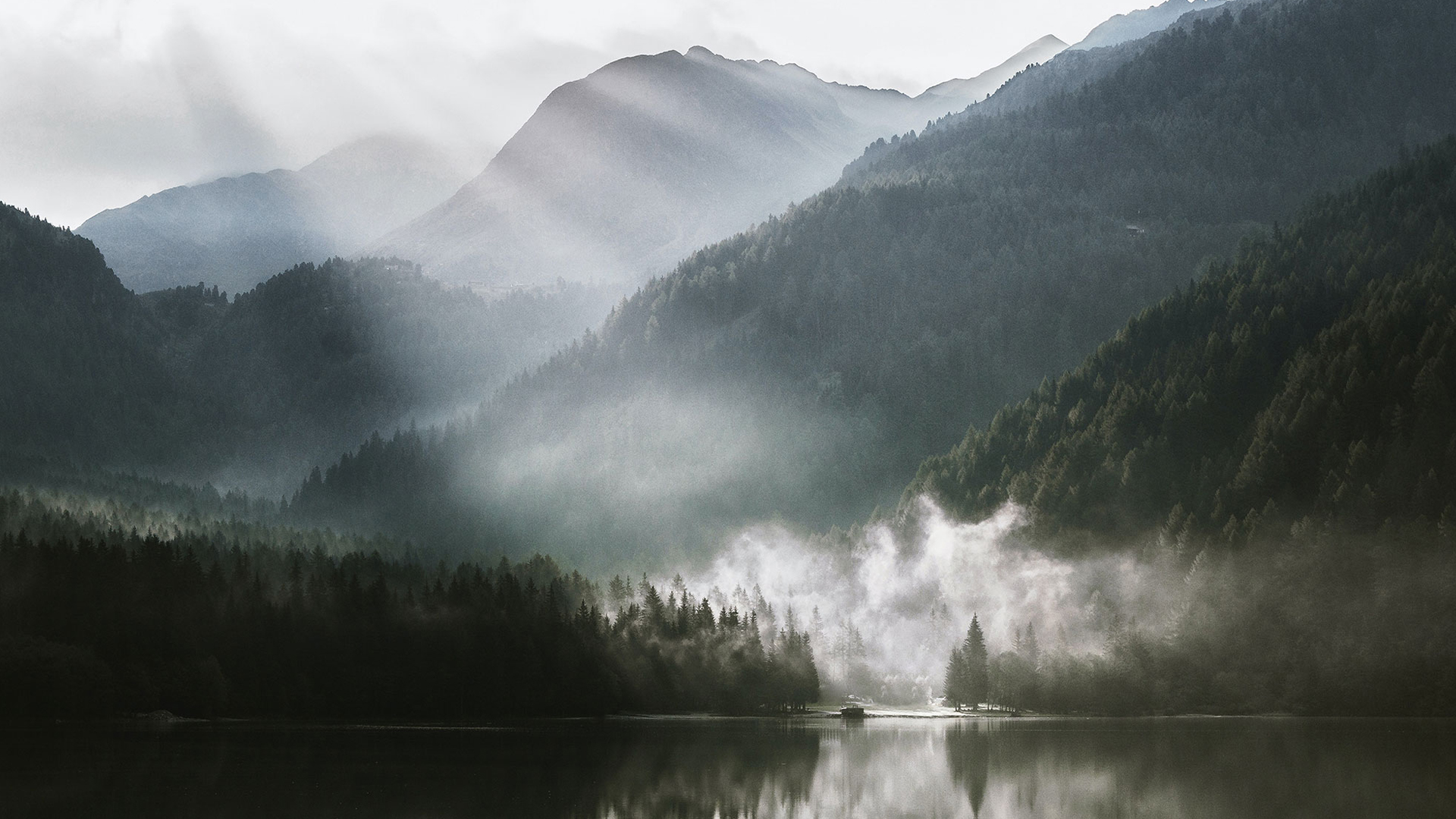 Nebel zieht durch ruhige Berglandschaft mit See in sanfter Morgenstimmung