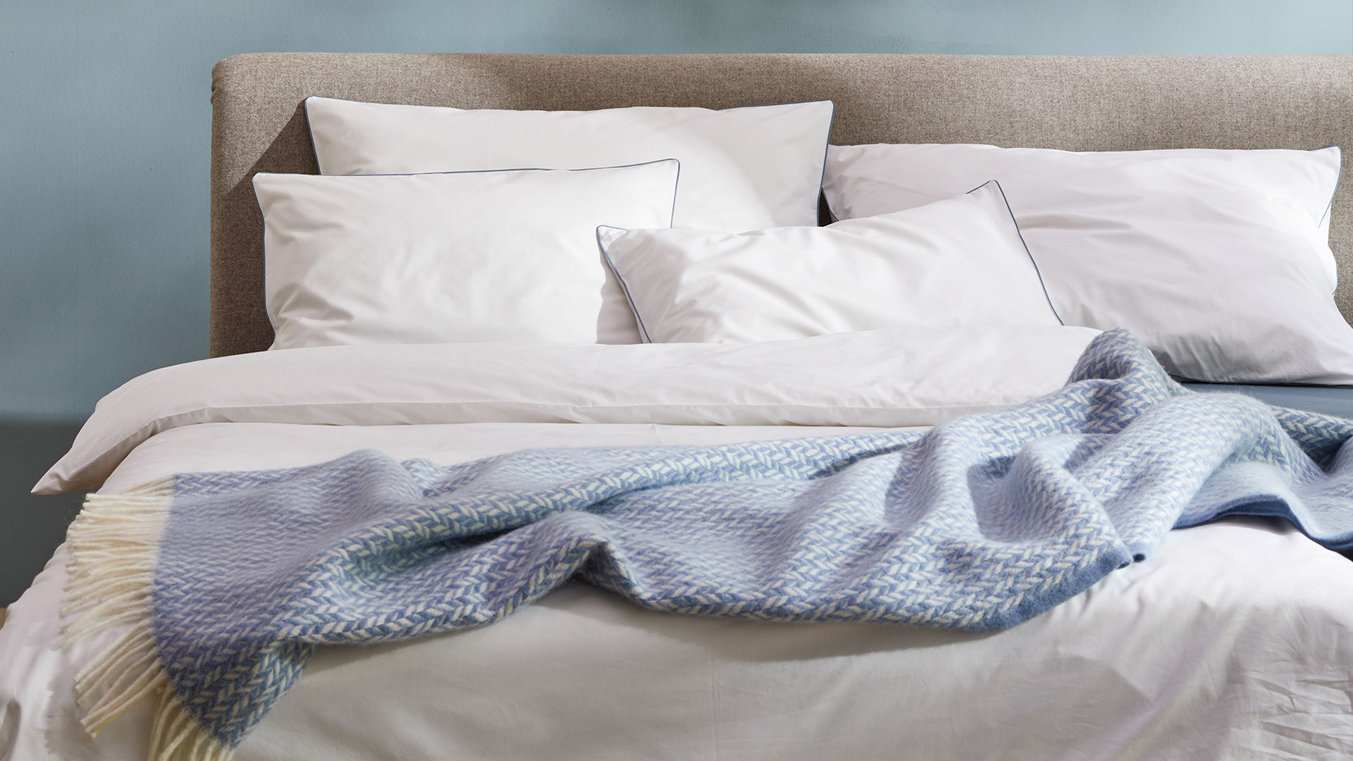 Blaue Wohndecke auf einer weißen Bettwäsche auf einem Bett liegend