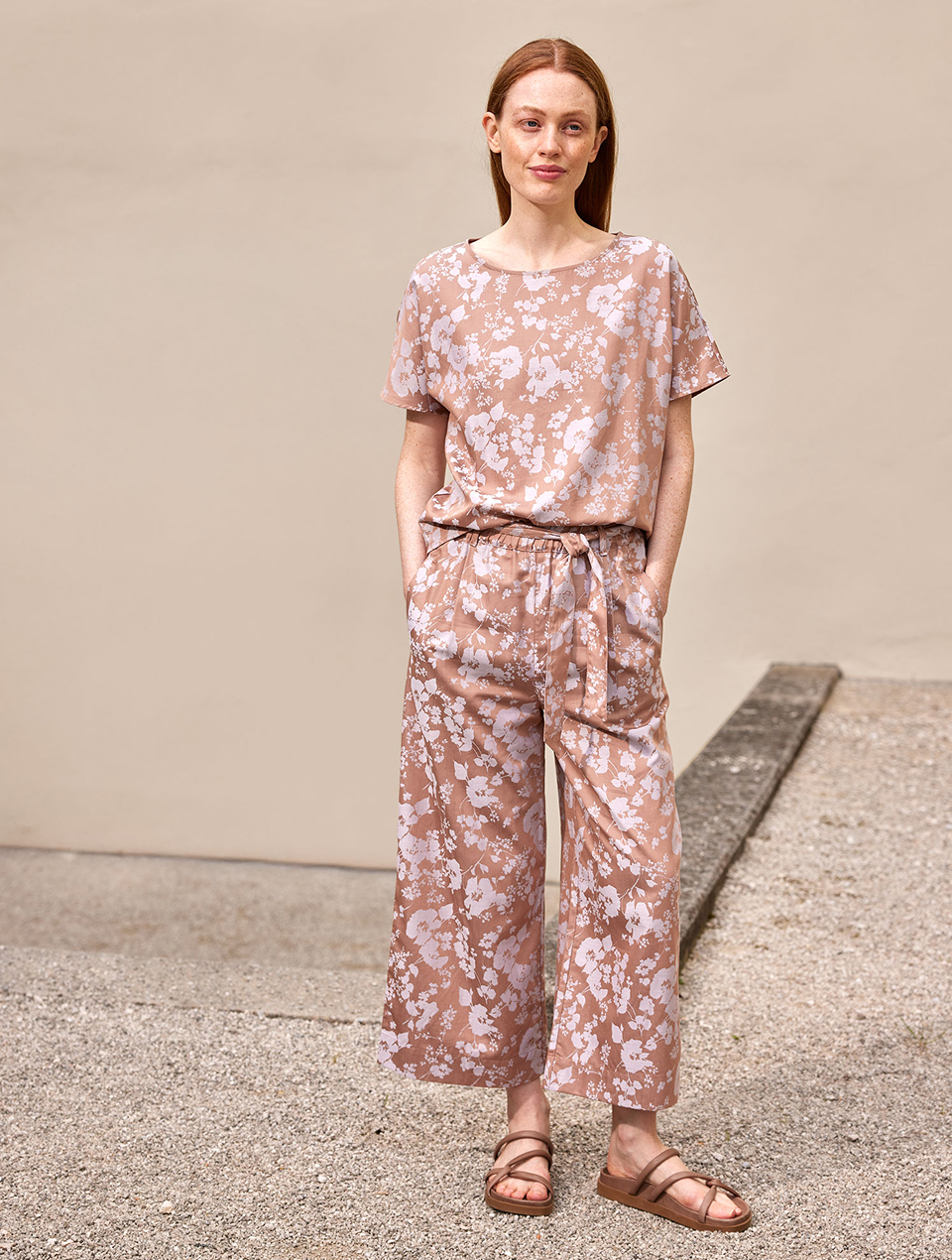 Frau trägt geblümtes Outfit mit Hose und Sandalen und steht im Außenbereich