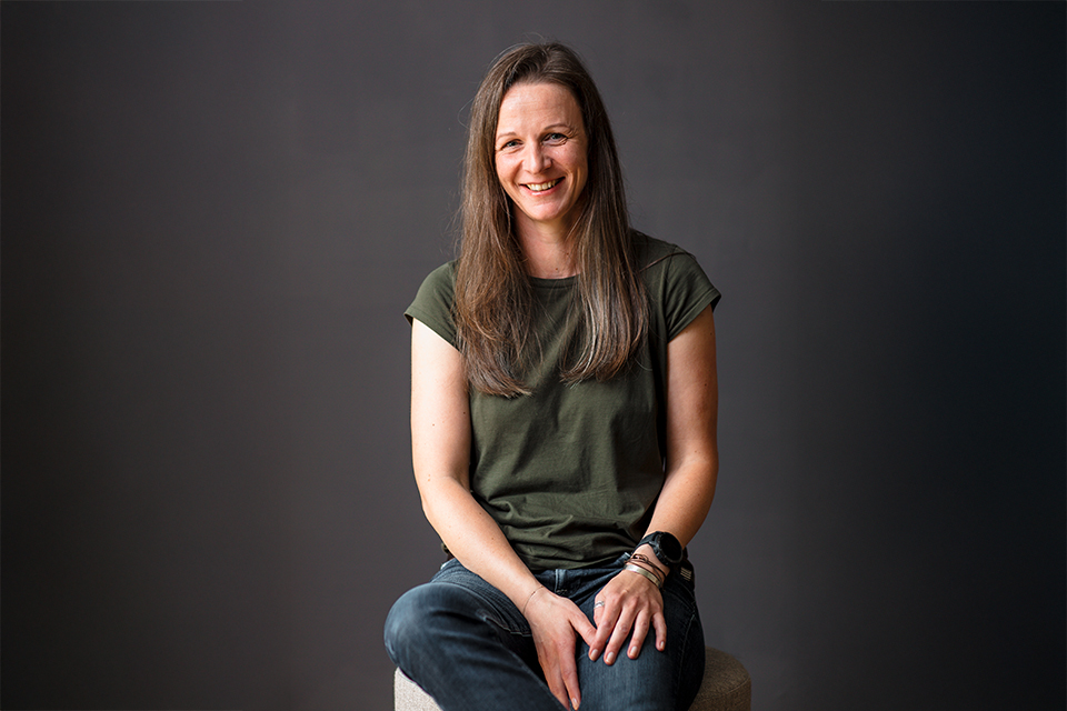 Frau sitzt entspannt vor dunklem Hintergrund und wirkt freundlich