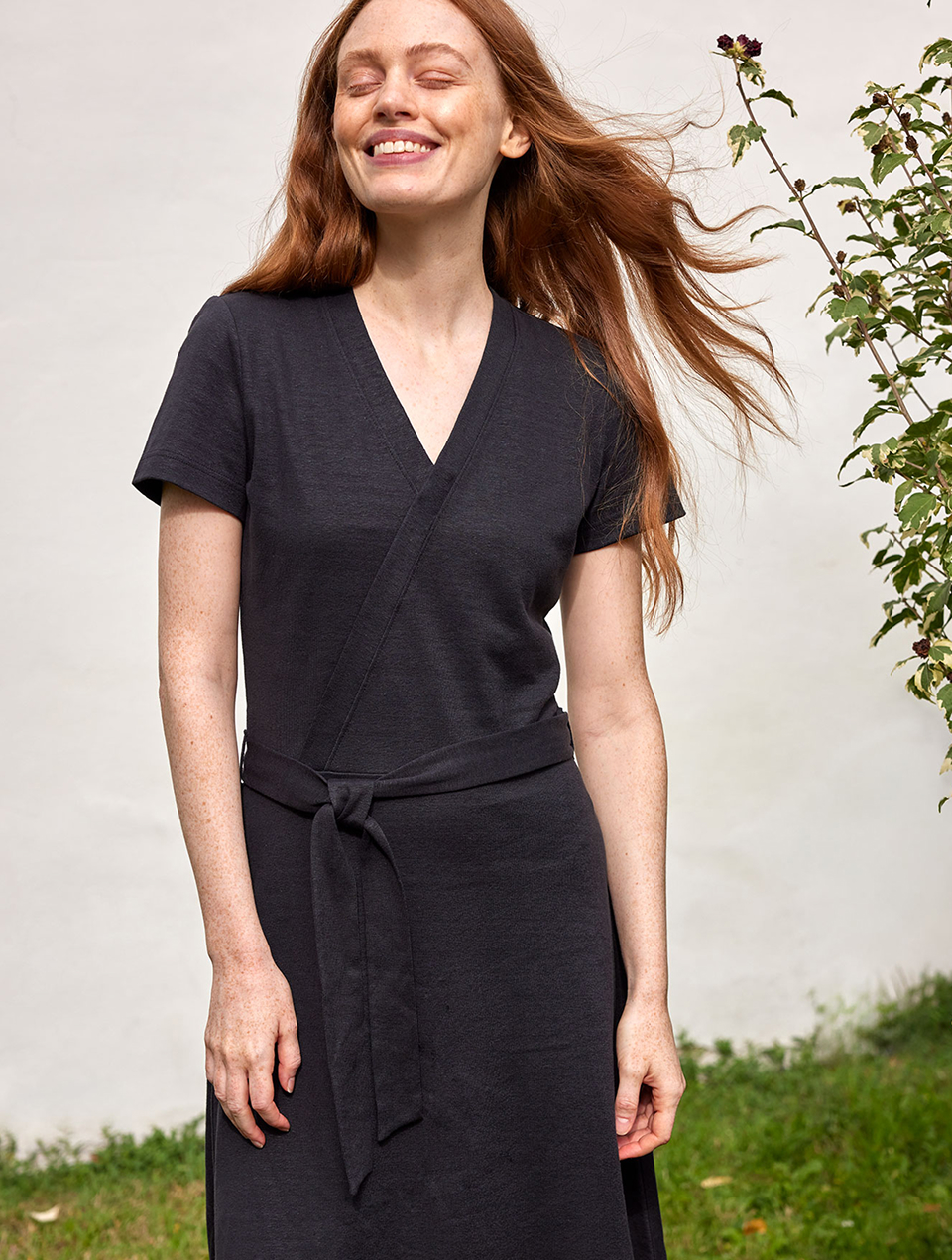 Frau trägt dunkles Kleid mit Wickeldetail und steht im Garten