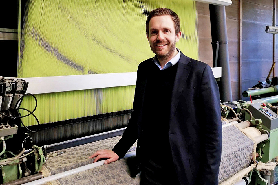 Mann steht lächelnd vor einer Webmaschine