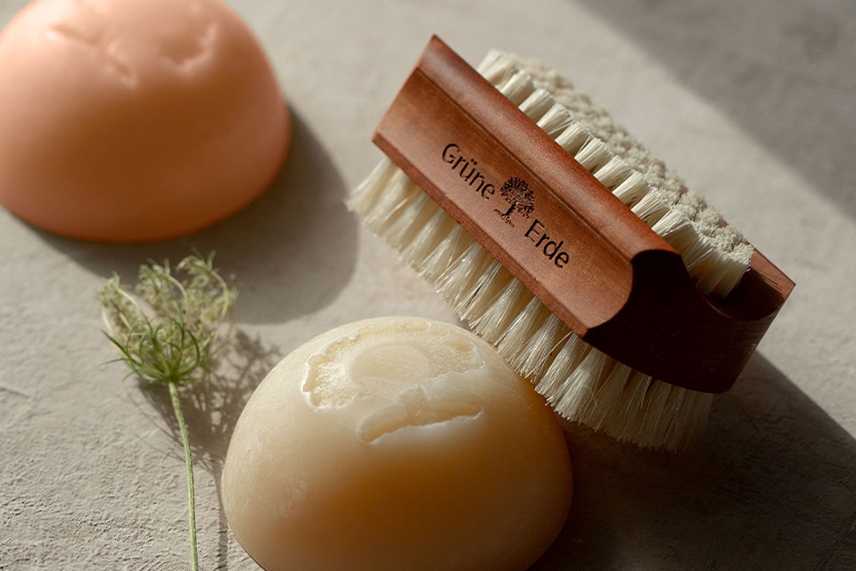 Naturseifen und Bürste liegen auf hellem Untergrund mit Kräutern dekoriert