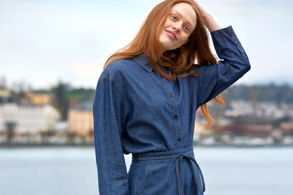 Frau in blauem Mantel steht am Wasserufer