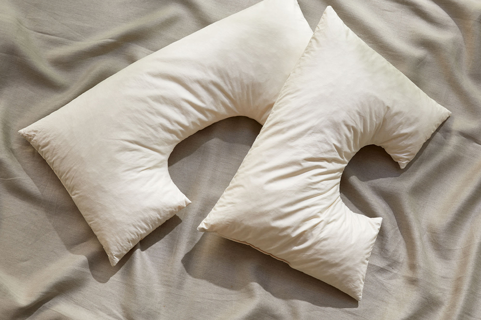 zwei Schulterkissen mit Ausnehmung liegen auf einem grauen Untergrund