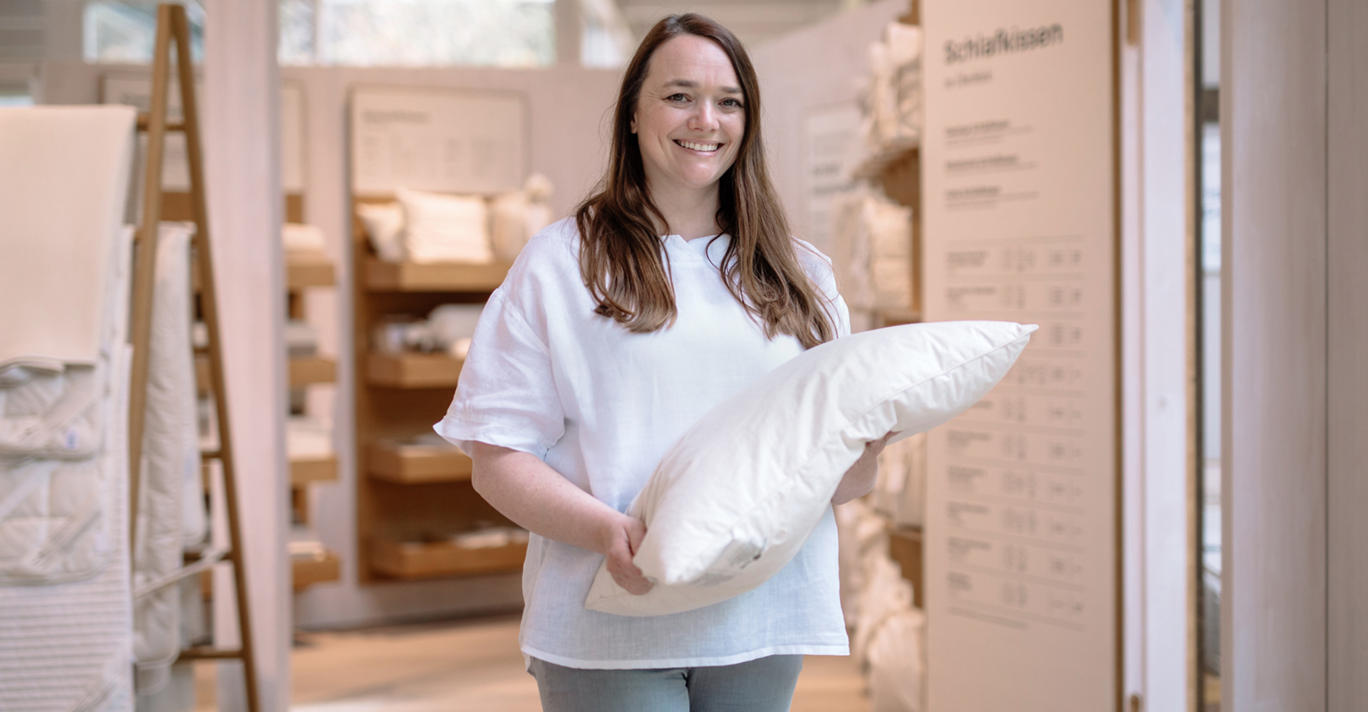 Freundliche Kundenberaterin mit einem weißen Schlafkissen in der Grünen Erde-Schlafwelt