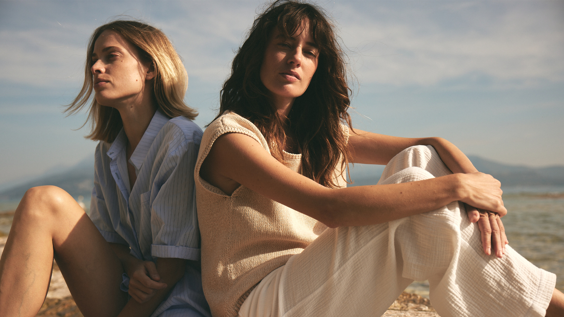 Zwei Frauen in nachhaltiger Kleidung sitzen entspannt am Strand