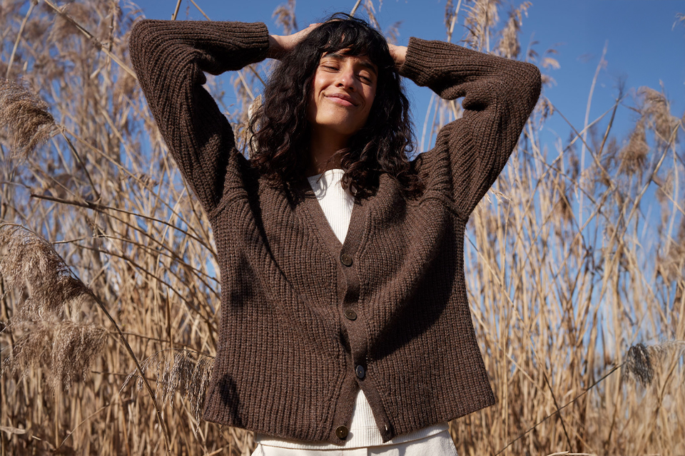 Frau in Strickjacke draußen in der Natur mit entspanntem Ausdruck