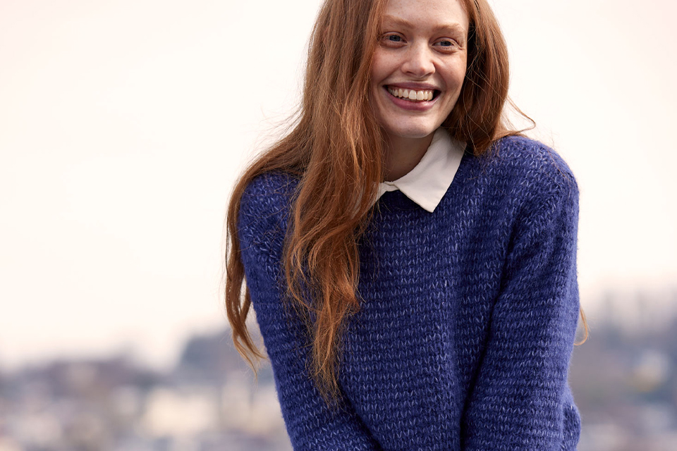 Lächelnde Frau im blauen Pullover mit unscharfem Hintergrund