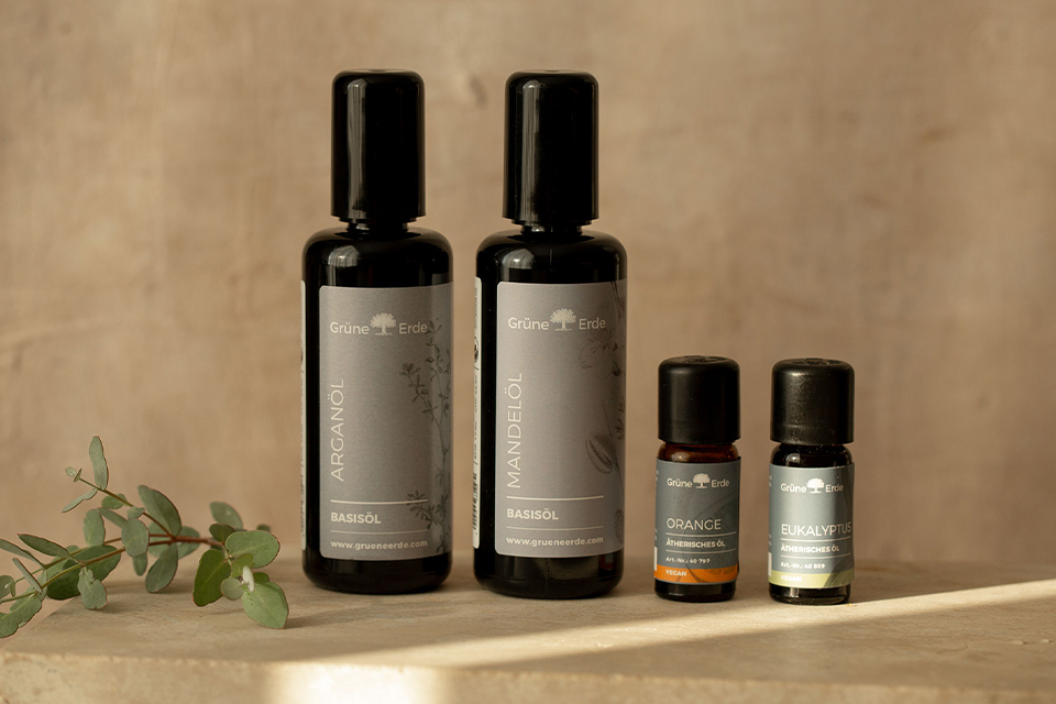 Zwei Basisöle und zwei Aromaöle neben einem dekorativen Zweig