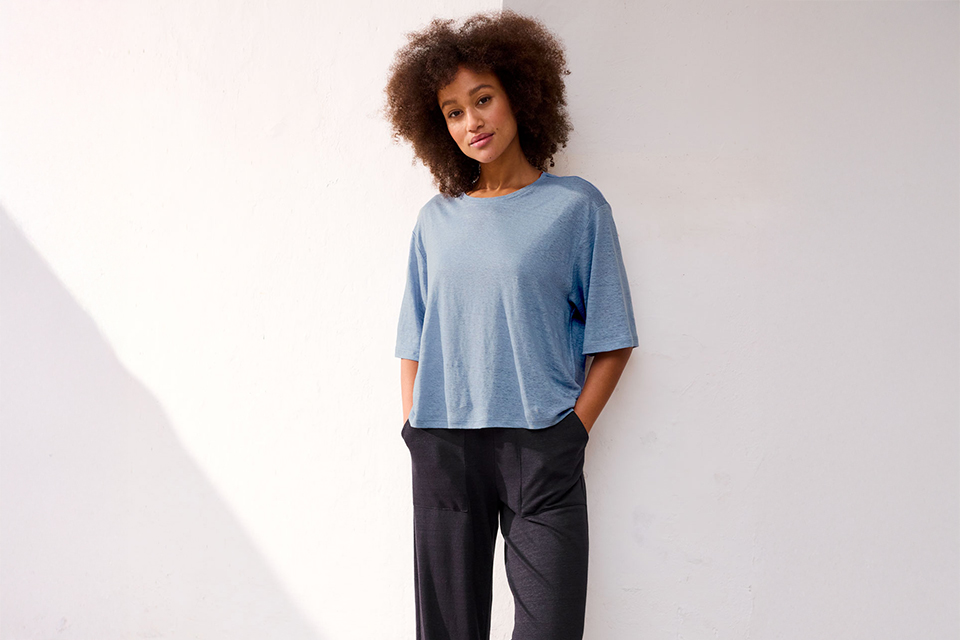 Frau in lockerem Outfit lehnt lässig an heller Wand