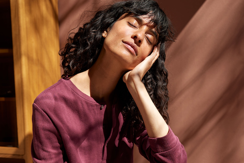 Person mit lockigem Haar entspannt im Sonnenlicht Augen geschlossen Kopf in der Hand