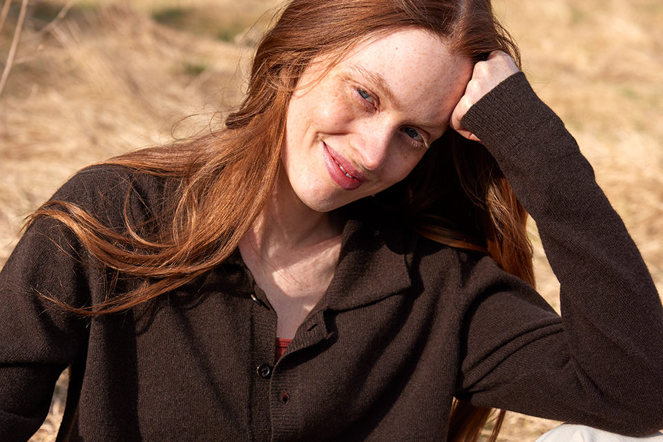 Eine Frau mit einem braunen Sweatshirt sitzt mit dKopf auf den Arm gestützt