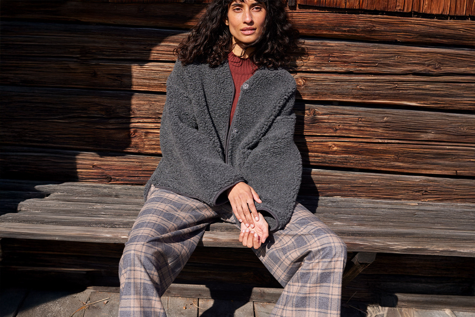 Frau sitzt entspannt vor Holzwand in moderner Kleidung