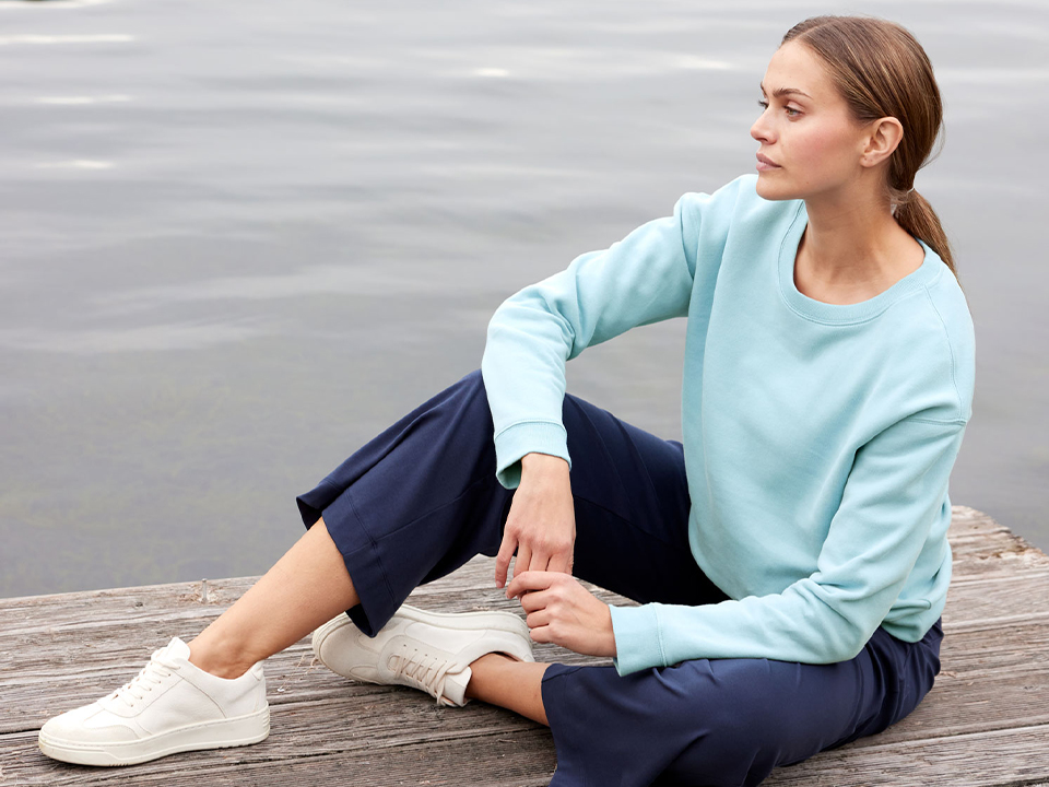 Frau sitzt an einem See in einem hellblauen Pullover