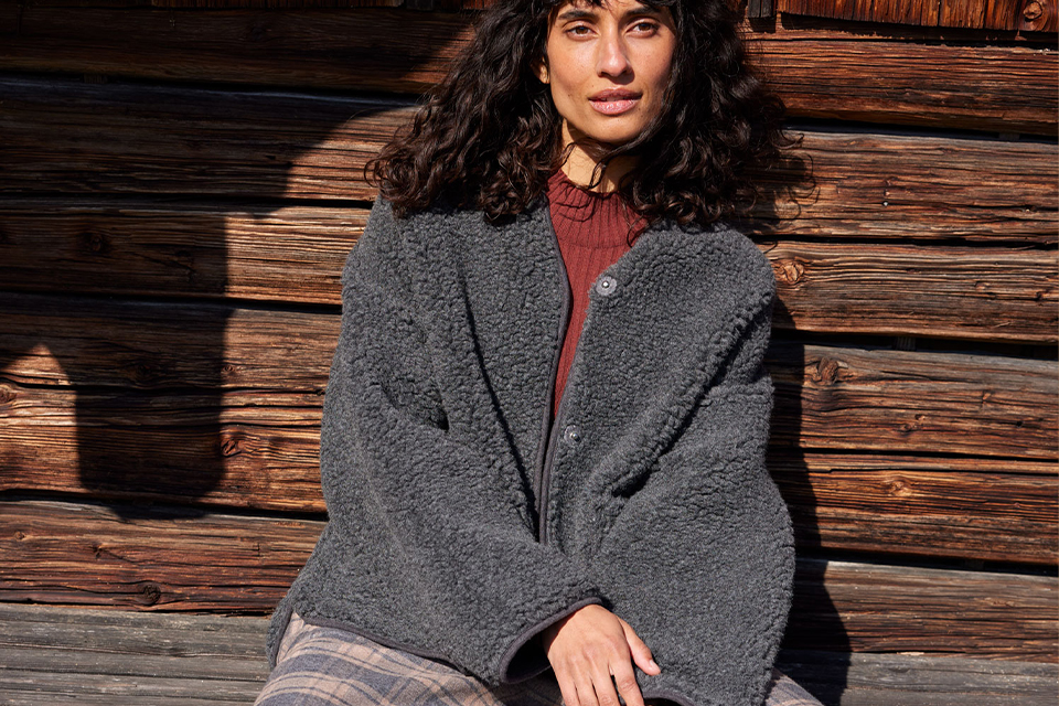 Frau sitzt entspannt vor Holzwand in moderner Kleidung