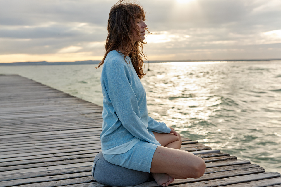 Eine Frau in blauer Kleidung sitzt auf einem Steg und blickt in die Ferne