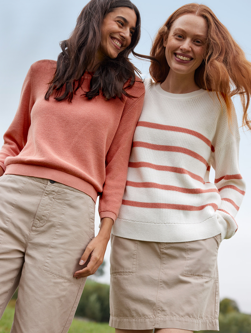 Zwei Frauen tragen Pullover in Weiß und Apricot mit beigen Unterteilen in natürlicher Umgebung