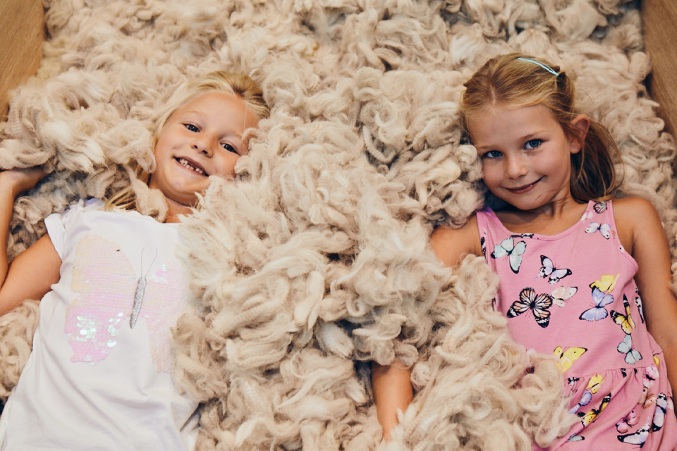 Zwei Mädchen liegen lachend in weichem Naturmaterial und spielen